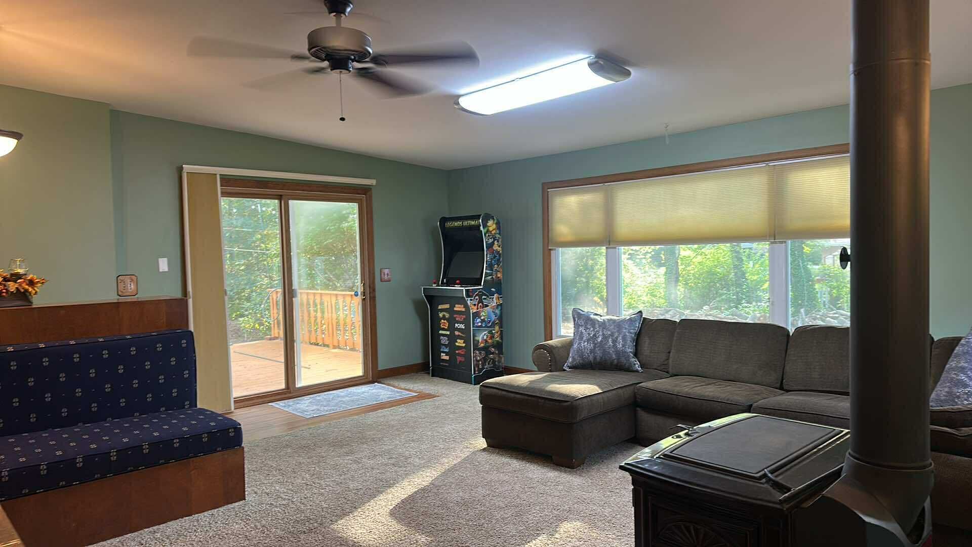 A living room with a sectional sofa, a small table, a ceiling fan, and a large window with blinds.