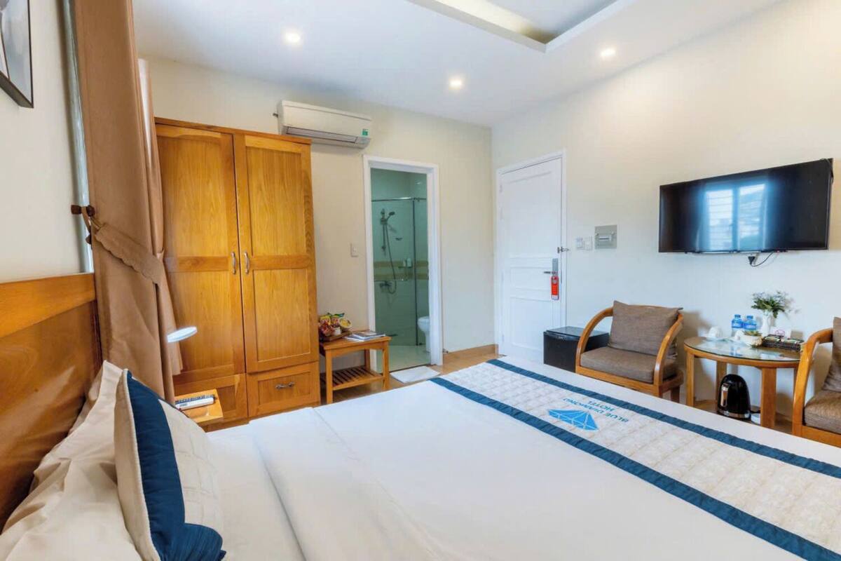 A hotel room with a large bed, wooden wardrobe, a television, a small table with a kettle, and a shower area.