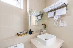 A bathroom with a white sink, a mirror, a towel rack, a telephone, and a small vase with flowers. - Blue Diamond Airport Hotel (Ho Chi Minh City)