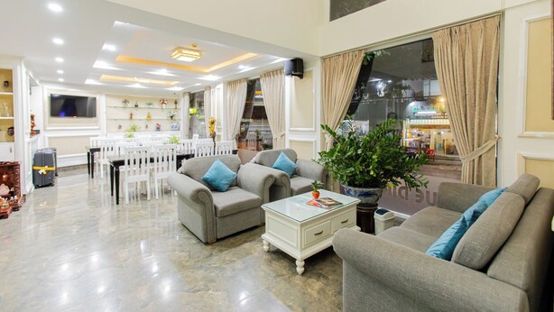 A spacious living area with grey sofas, a coffee table, and a dining area with white chairs and a TV. - Blue Diamond Airport Hotel (Ho Chi Minh City)