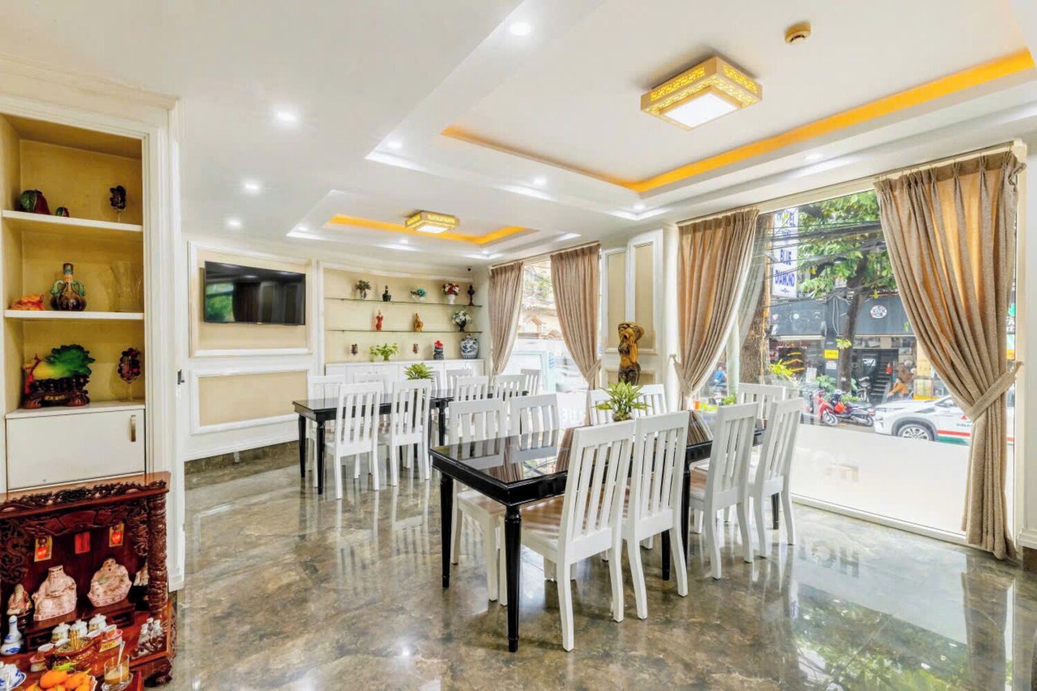 A dining area with a black table and white chairs, a TV on the wall, and a view of the street outside.