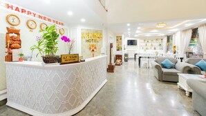 A hotel reception area with a reception desk, a 'Happy New Year' sign, a 'Blue Diamond Hotel' sign, and a dining area with a white table and grey sofas. - Blue Diamond Airport Hotel (Ho Chi Minh City)