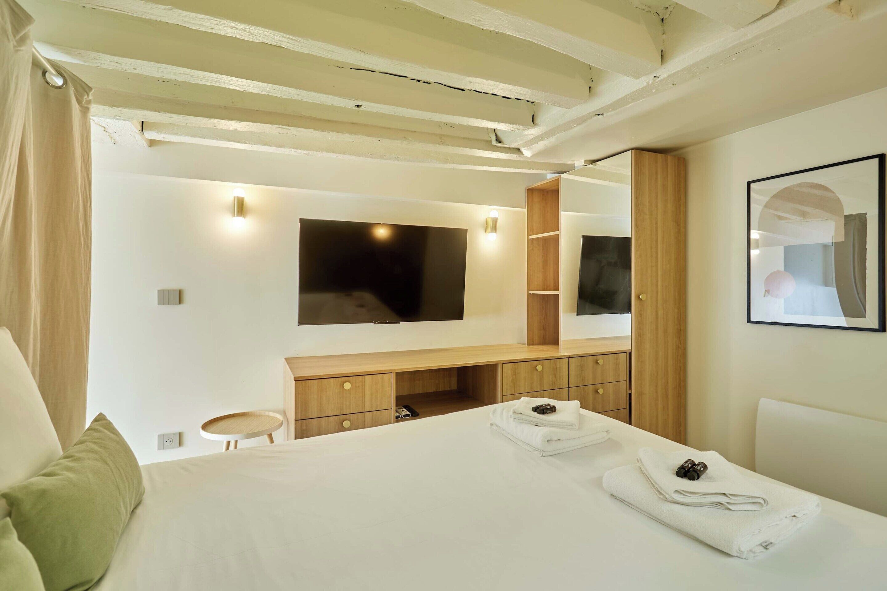 Ein modernes Hotelzimmer mit einem Bett, einem an der Wand befestigten Fernseher, einem Holztisch und einem kleinen runden Tisch.