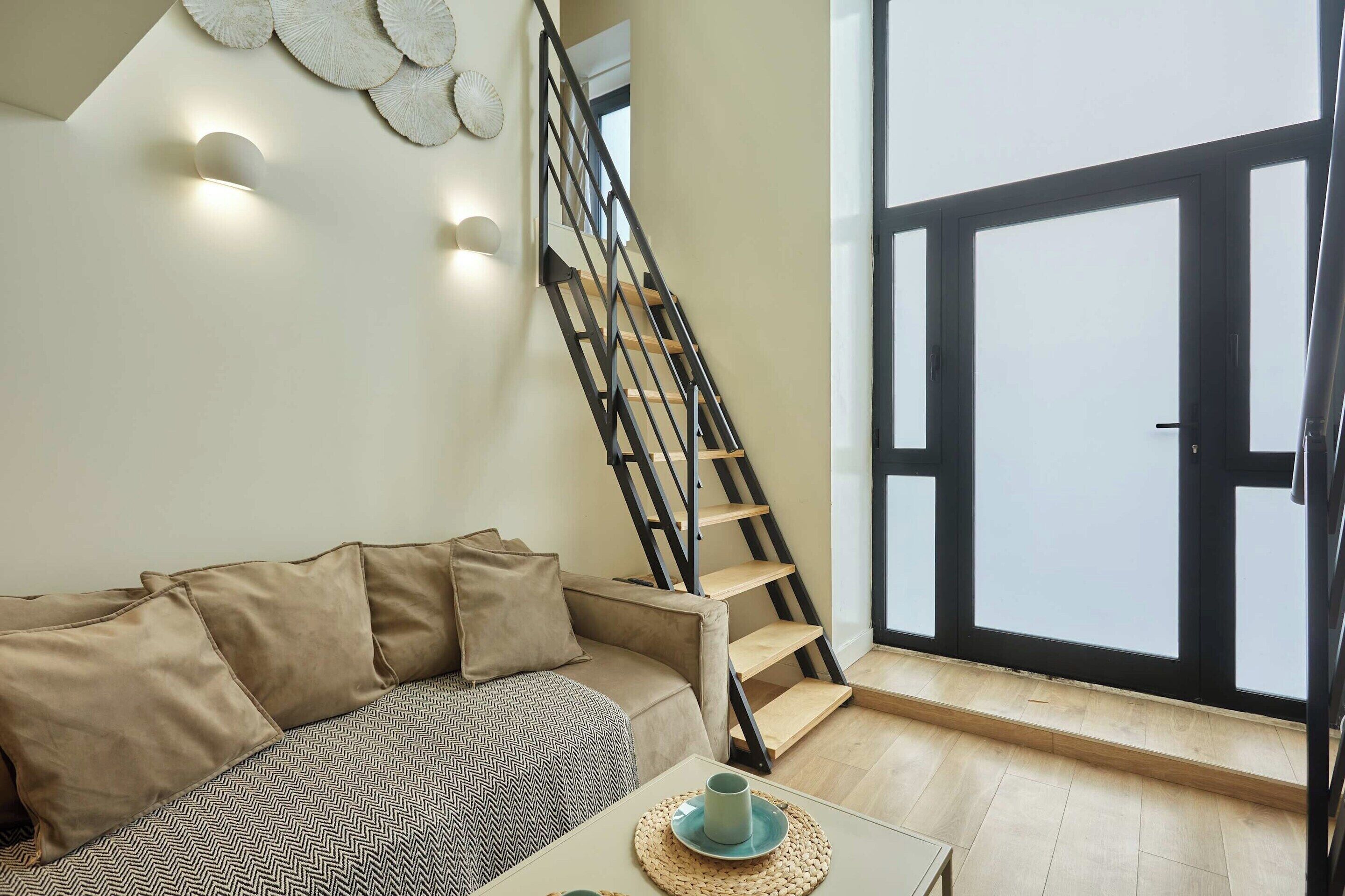 A modern living room with a sofa, a coffee table, and a staircase with a black railing.