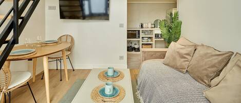 Una sala de estar moderna con un sofá, una mesa de comedor con sillas, un televisor montado en la pared y una escalera.