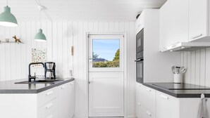 A modern kitchen with white cabinetry, a coffee maker, pendant lights, and a view through a door.