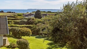 A residential area with a view of the sea, featuring houses, a garden, and a pathway.