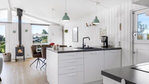 A modern kitchen with a central island, white cabinetry, pendant lighting, and a wood-burning stove.