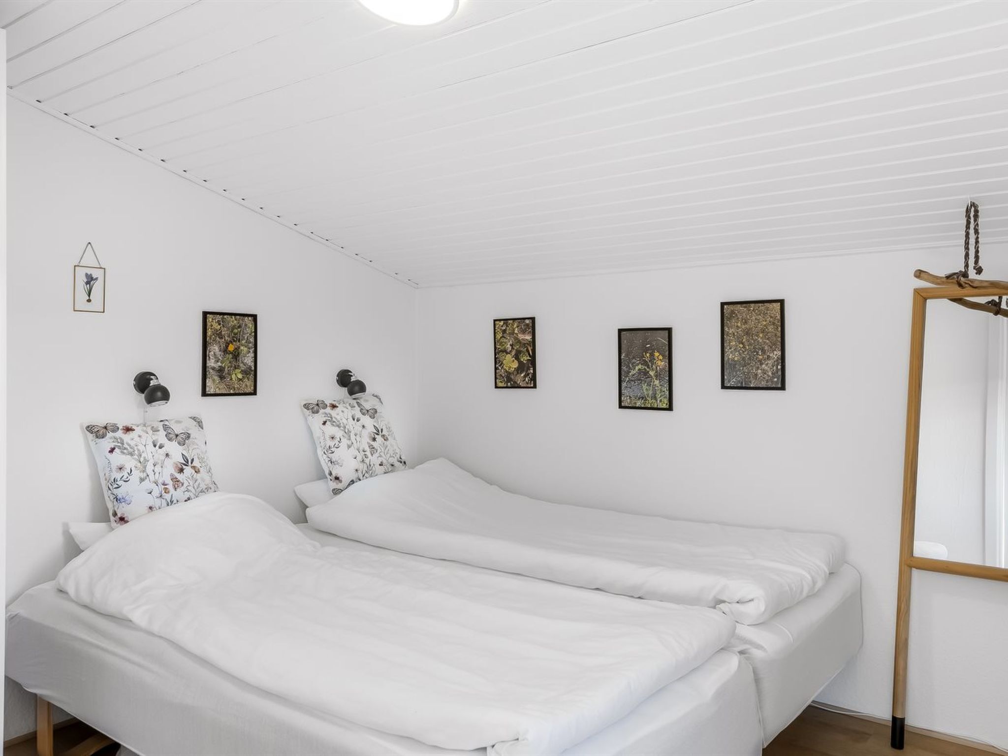 Een kamer met twee bedden, witte beddengoed, een houten hoofdbord en vier ingekaderde foto's aan de muur.