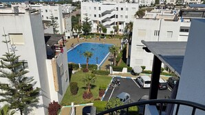 Área residencial com piscina cercada por vegetação e edifícios brancos.