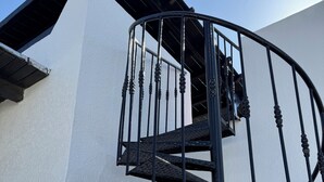 Escada em espiral com balaústres ornamentados em frente a uma parede branca.
