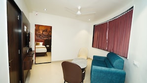 A compact room with a bed, a blue sofa, a dining table with a chair, and a ceiling fan. - Kings Executive (Tuljapur)