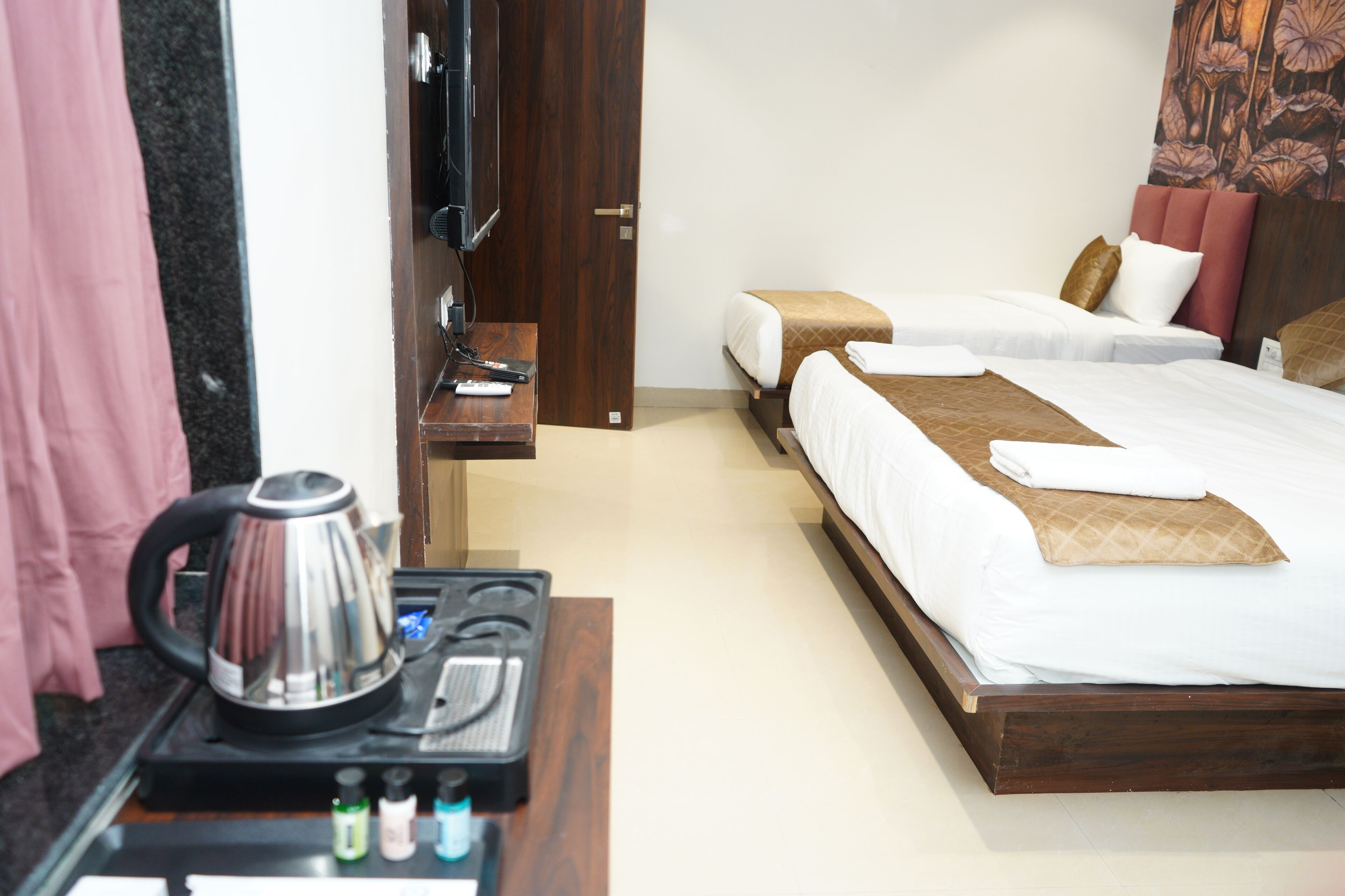 A hotel room with two beds, a wooden headboard, a TV, a kettle, and a small table with toiletries.