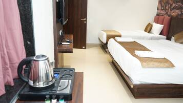 A hotel room with two beds, a wooden headboard, a TV, a kettle, and a small table with toiletries.