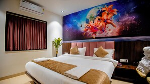 A hotel room with a large bed, a nightstand, a wall-mounted air conditioner, and a ceiling light. - Kings Executive (Tuljapur)