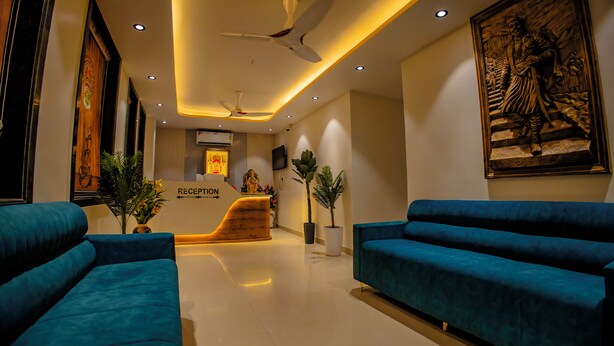 A modern reception area with a reception desk, blue sofas, ceiling fans, and a large wall sculpture. - Kings Executive (Tuljapur)