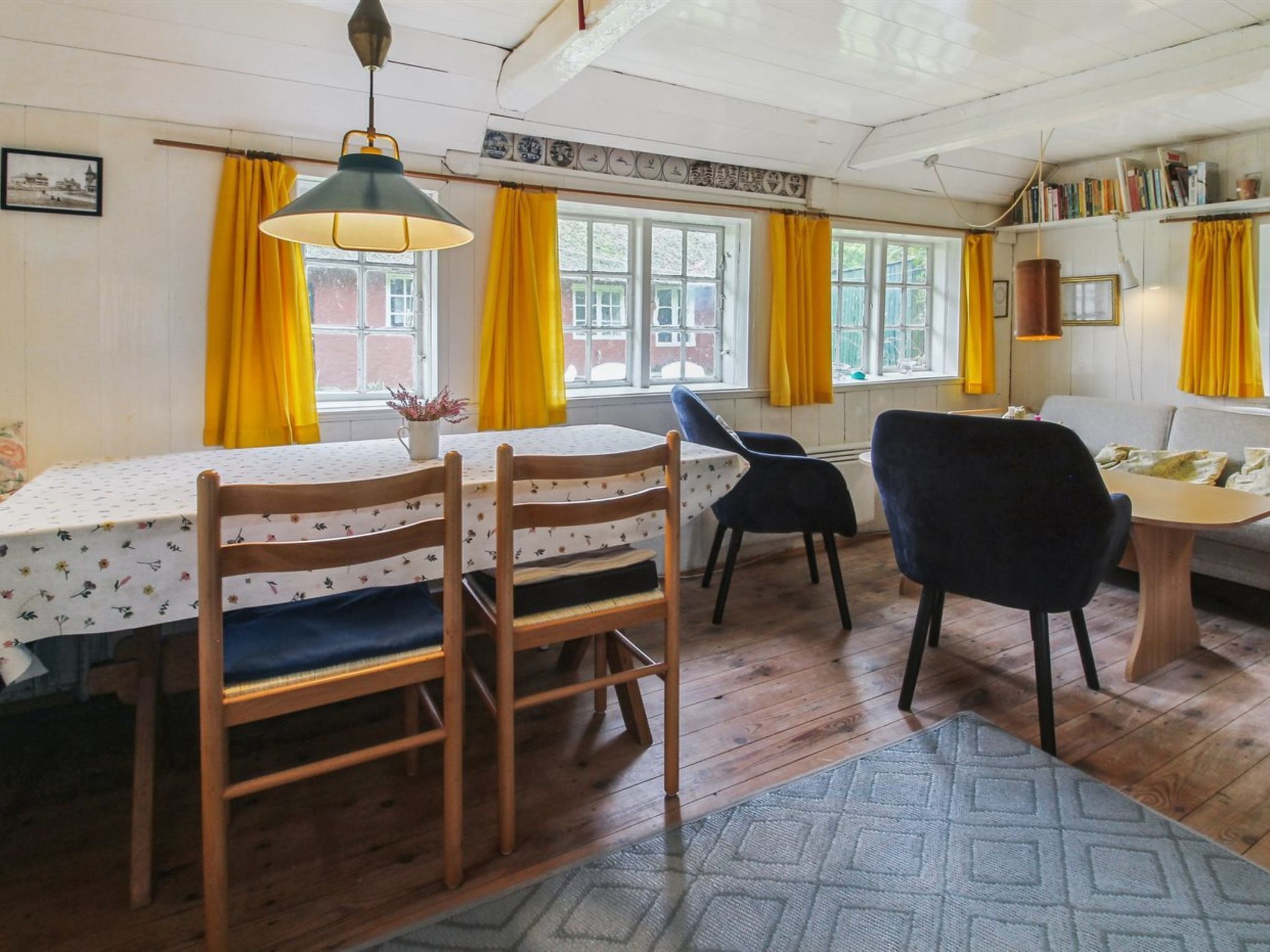 Un coin repas avec une table et des chaises, des rideaux jaunes et une lampe suspendue.