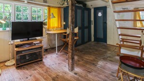 Interior rústico de una cabaña con piso de madera, televisor, escritorio y silla.