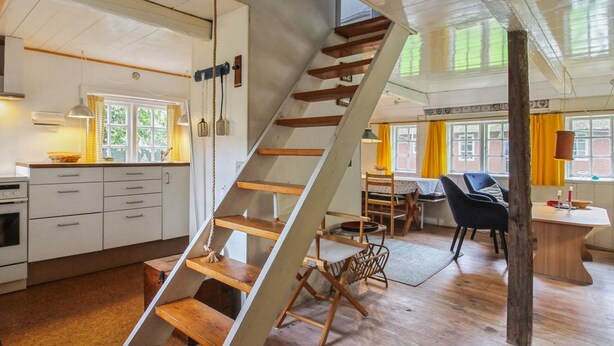 Una cocina moderna con armarios blancos, una escalera de madera y un comedor con mesa y sillas.