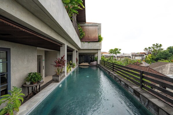 A modern building with a swimming pool, potted plants, and a balcony with greenery. - Duur Apartments by Betterplace (Seminyak)