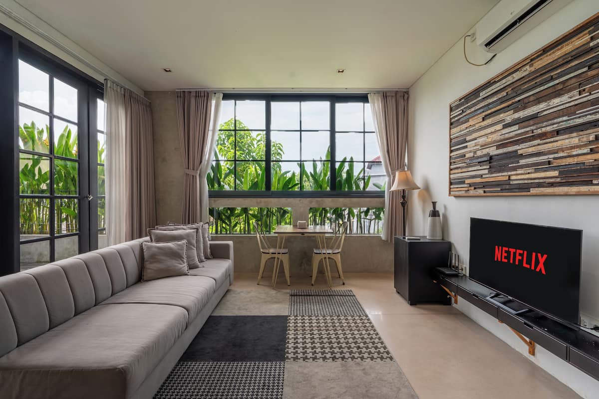 A modern living room with a sofa, a dining table with chairs, a TV, and a large window with curtains.