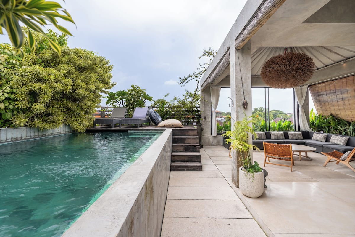A modern outdoor pool area with a concrete edge, a wooden staircase, and a seating area with a sofa and chairs.