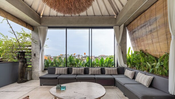 Ein moderner Außenbereich mit einem runden Tisch, gepolsterten Sofas und Blick auf die Stadt durch große Fenster.