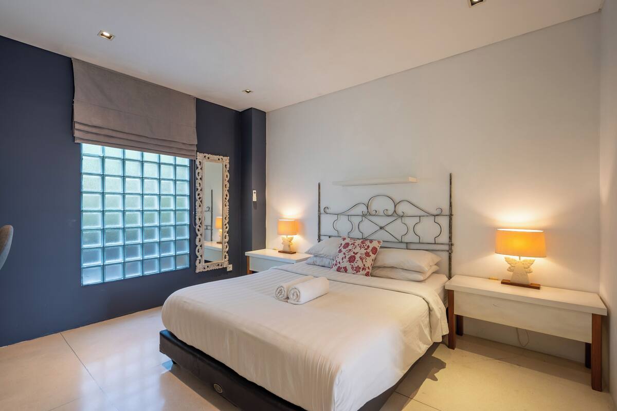 A bedroom with a large bed, bedside tables with lamps, a window with curtains, and a headboard.
