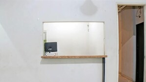 Une pièce avec un mur blanc, une étagère en bois et une porte donnant sur une autre pièce.