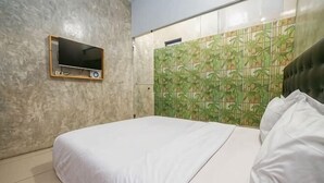 Une chambre avec un lit, un téléviseur fixé au mur et un mur décoré d’un motif.