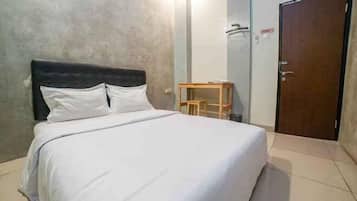 A single bed with a headboard, a wooden side table, and a door in a room with a plain wall and tiled floor.