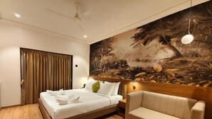 Une chambre d’hôtel avec un lit, un canapé, une petite table, un tableau au mur et un ventilateur de plafond.