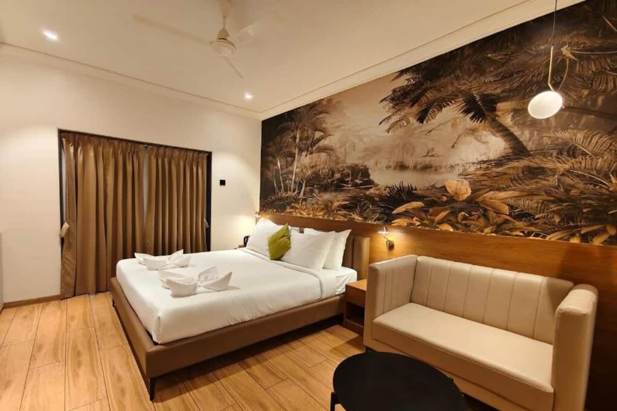 Camera d'albergo con un letto, un divano, un tavolino, un quadro appeso al muro e una ventola a soffitto.