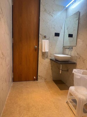 Un baño con puerta de madera, paredes de mármol, un lavamanos blanco y un espejo.
