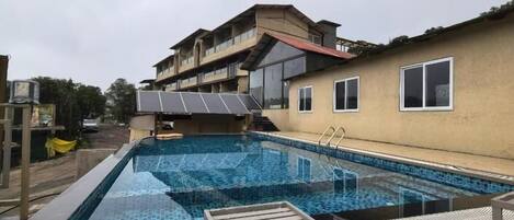 A swimming pool with a sun deck, a building with balconies, and a clear sky.