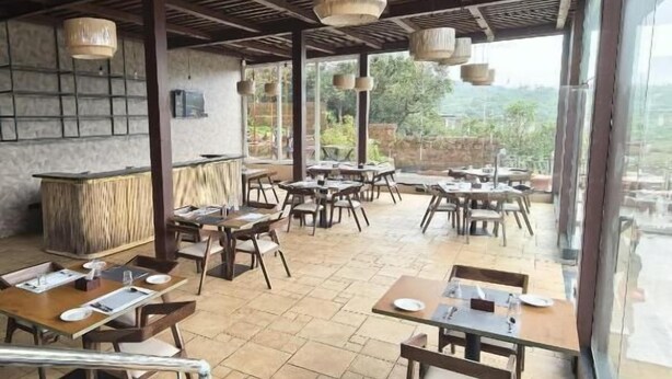 Un espace de restauration en plein air avec des tables et des chaises en bois, des luminaires suspendus et une vue sur l’extérieur.