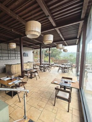 An outdoor dining area with wooden tables and chairs, hanging light fixtures, and a view of the outdoors. - Regenta Z Mahabaleshwar (Mahabaleshwar)