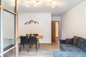 Een moderne woonkamer met een houten eettafel, twee stoelen, een grijze bank en een wandlamp.