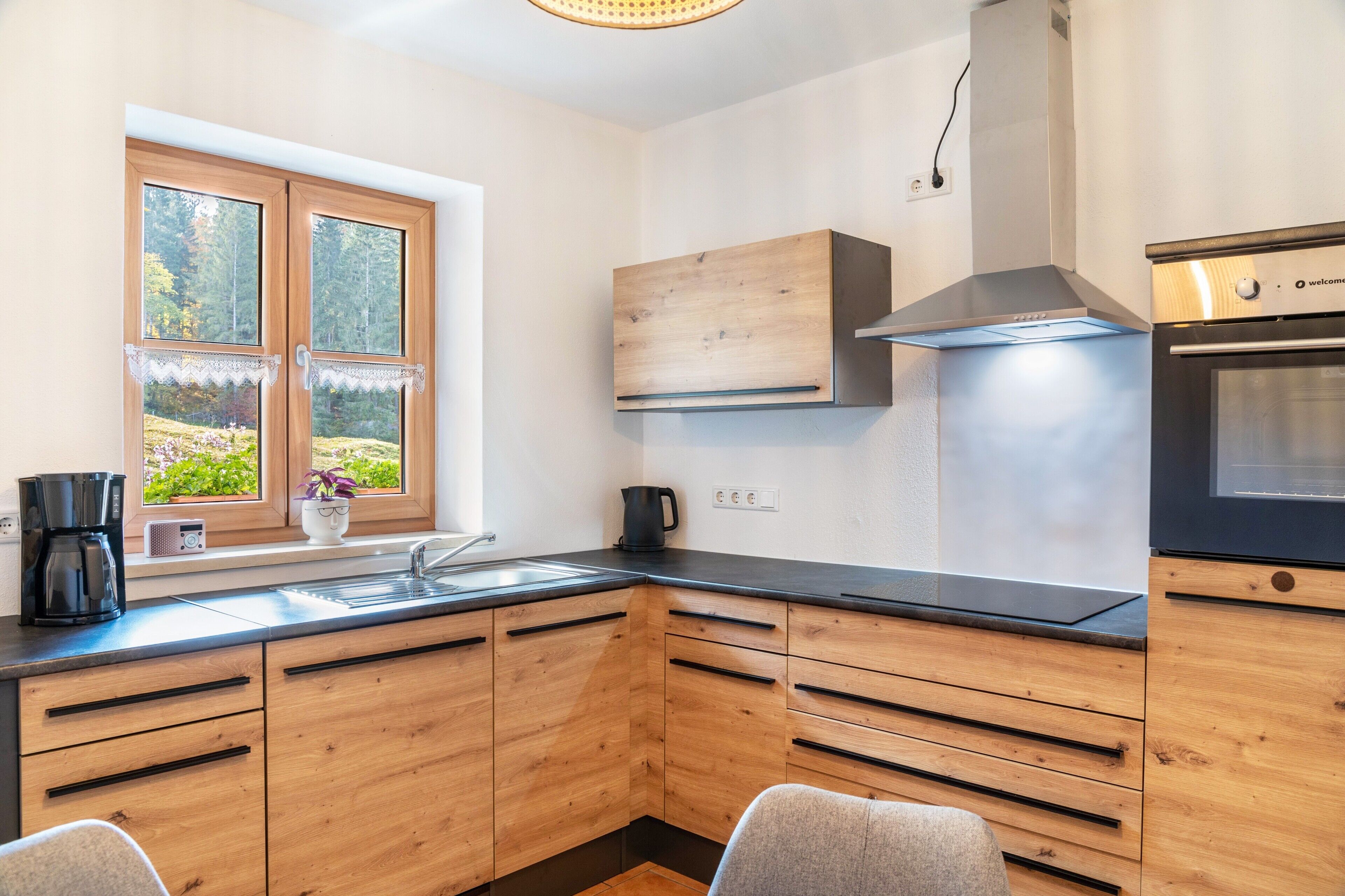 A modern kitchen with wooden cabinets, a built-in oven, and a window with a view of greenery.