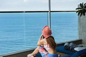 Een kamer met een groot raam met uitzicht op de zee, een blauwe bank en een potplant.