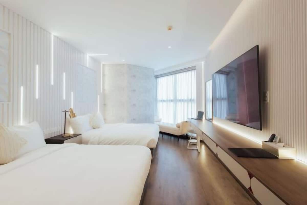 Een moderne hotelkamer met twee bedden, een grote televisie en een bureau.