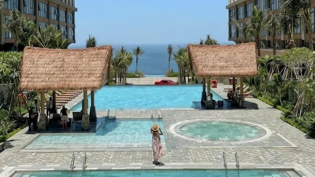 Zwembadgedeelte met uitzicht op de oceaan, een loungeruimte met rieten parasols en een rond waterornament.