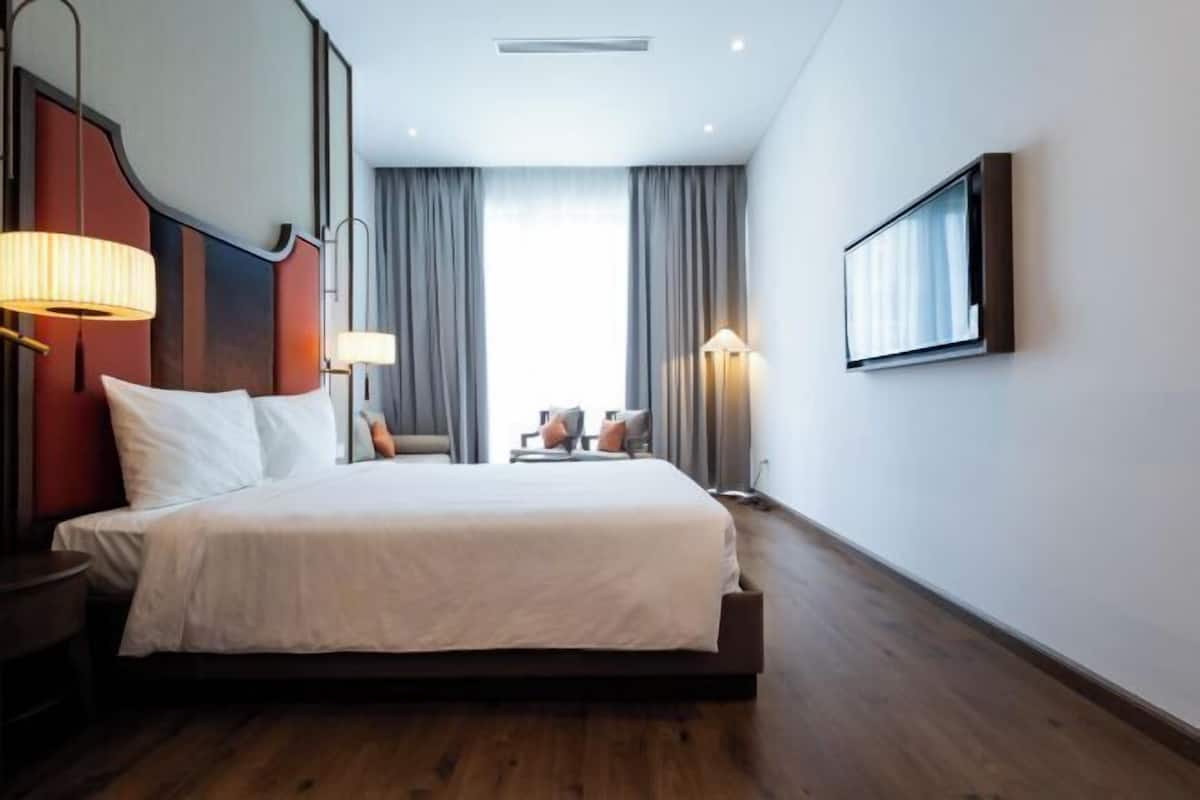 Hotelkamer met een groot bed, een bureau, een stoel, een lamp, een televisie en een raam met gordijnen.
