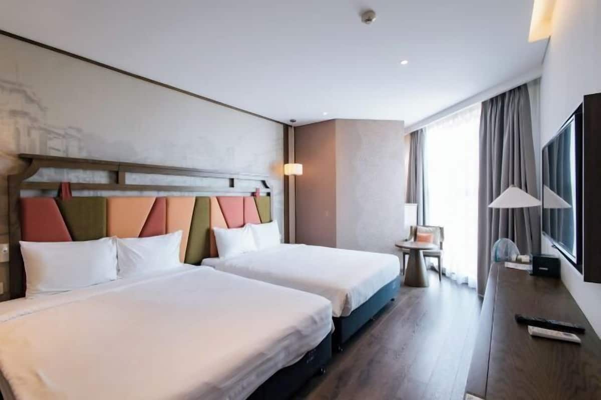 Een hotelkamer met twee bedden, een tafeltje, een stoel, een televisie en een raam met gordijnen.