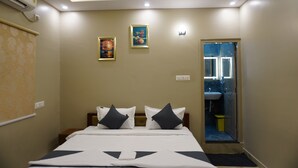 A hotel room with a bed, two pillows, a wall-mounted air conditioner, a ceiling light, and a door leading to a bathroom. - Stazy Suites - Kammanhalli (Bengaluru)