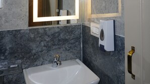 A bathroom with a marble wall, a white sink, a mirror with a light, and a hand dryer. - Stazy Suites - Kammanhalli (Bengaluru)