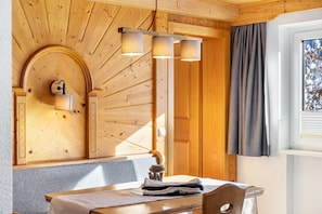 Un interior de madera con una mesa, sillas, una lámpara colgante y una ventana con cortinas.