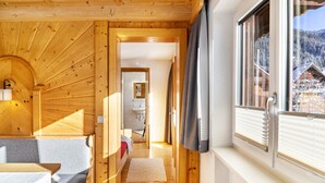 A wooden cabin interior with a cozy seating area, a hallway leading to a bathroom, and a window with a snowy mountain view. - Apartment 'Gaichtspitze - 8' with Mountain View, Private Balcony and Wi-Fi (Nesselwängle)