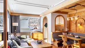 Ein gemütliches Zimmer mit einem Holztisch, einer Couch, einer Bank und einem Fenster mit Bergblick.