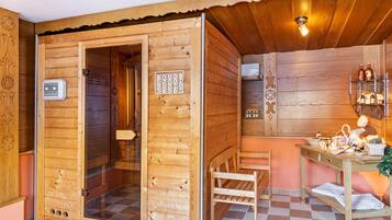 A wooden sauna room with a glass door, a bench, a table with bottles, and a wall-mounted shelf.
